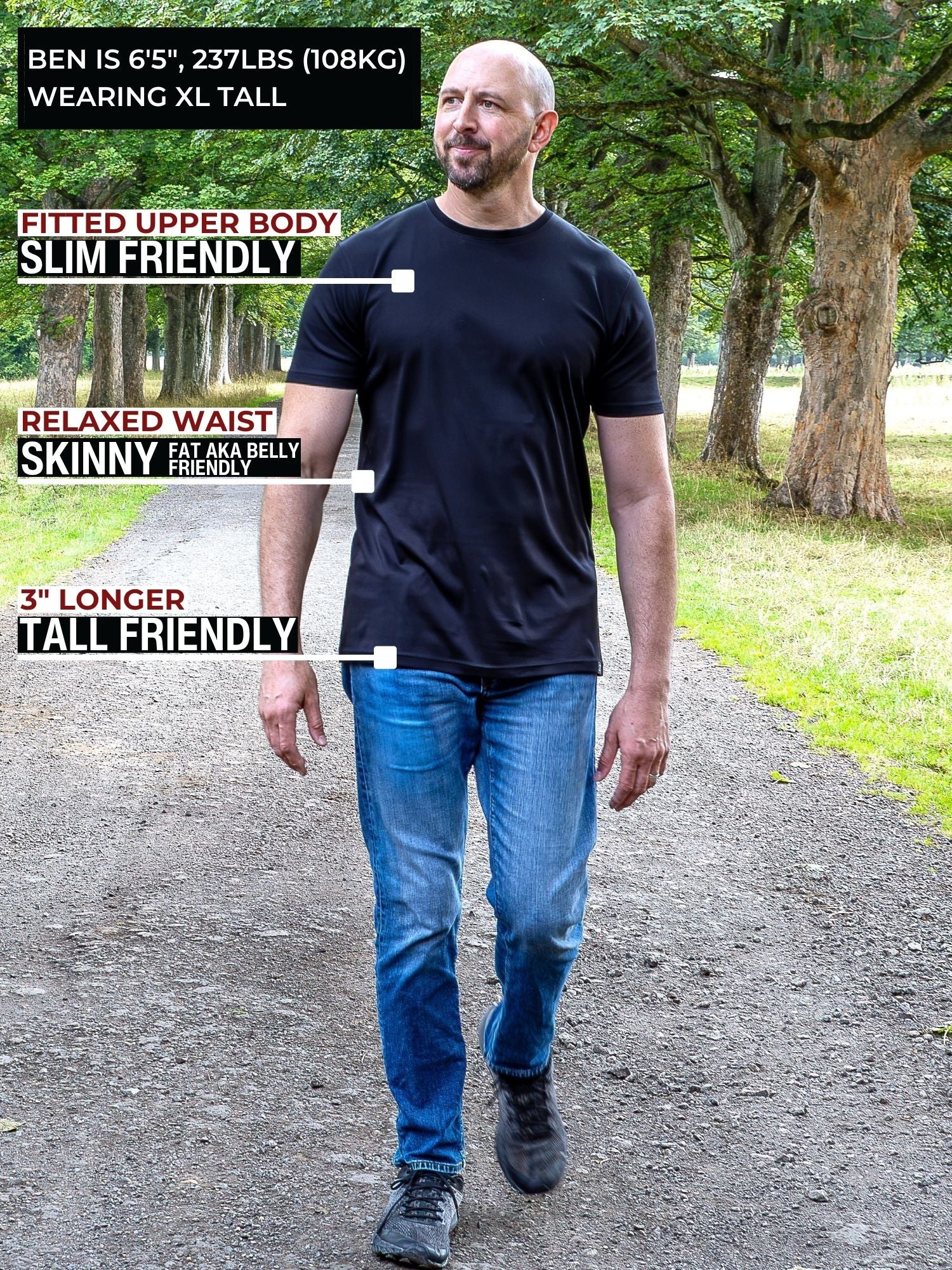 A tall man standing on a park path wearing a black fitted short-sleeve t-shirt and blue jeans, with text callouts describing the shirt's fit and length.
