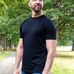 An upper body shot of a tall slim guy in a park wearing an XL tall and slim fitting mercerised t-shirt in black.