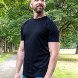 An upper body shot of a tall slim guy in a park wearing an XL tall and slim fitting mercerised t-shirt in black.