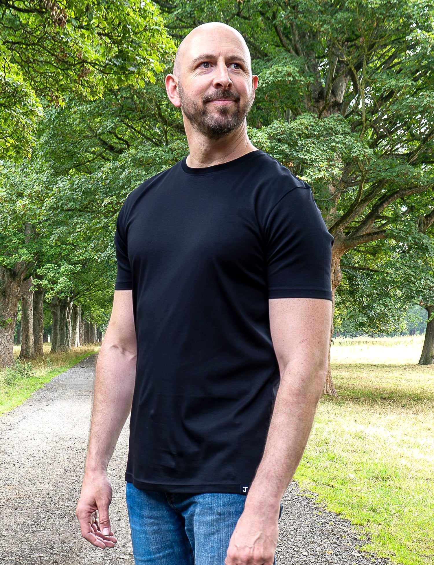 An upper body shot of a tall slim guy in a park wearing an XL tall and slim fitting mercerised t-shirt in black.