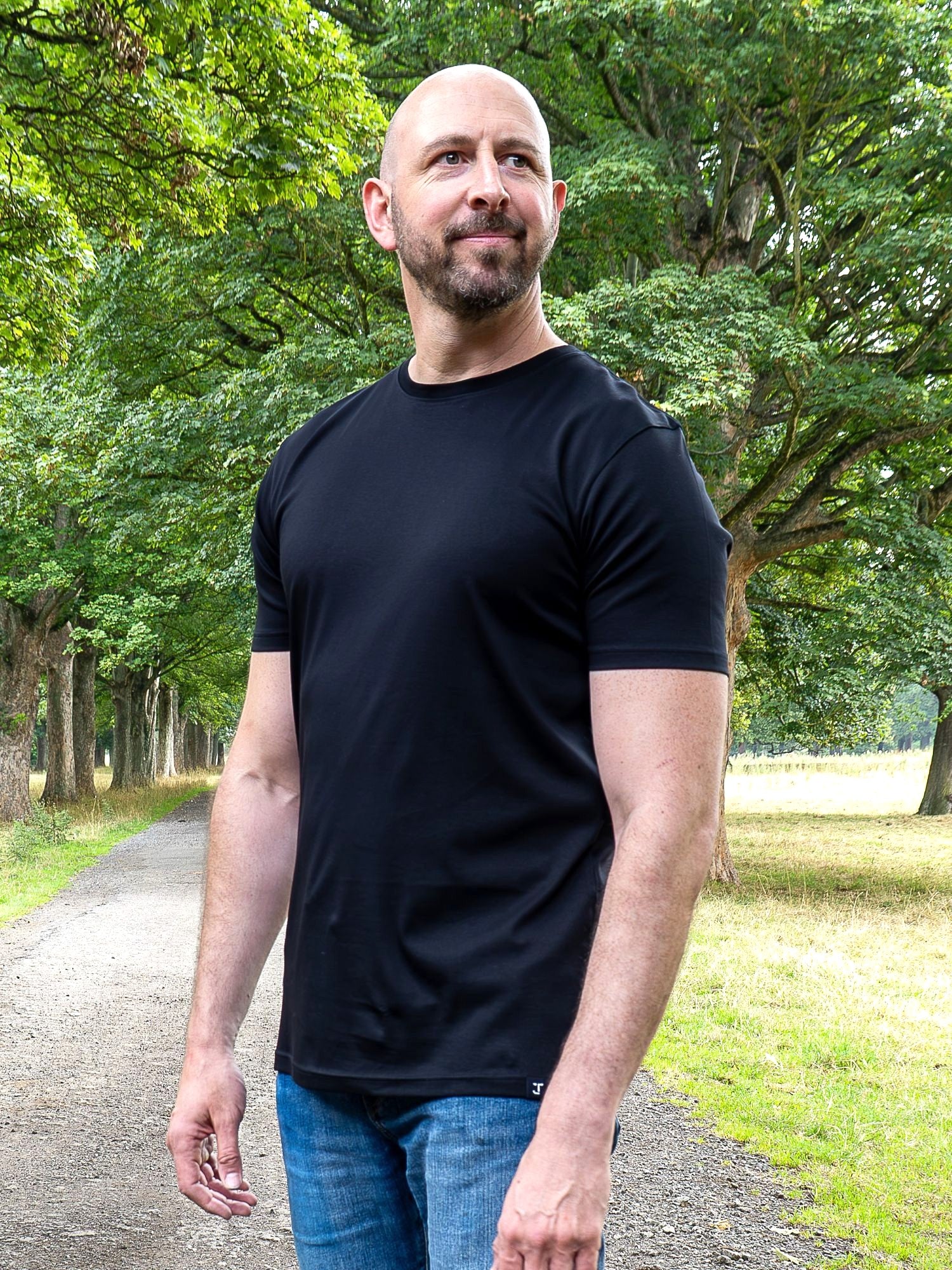 An upper body shot of a tall slim guy in a park wearing an XL tall and slim fitting mercerised t-shirt in black.