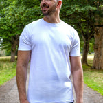 An upper body shot of a tall slim guy in a park wearing an XL tall and slim fitting mercerised t-shirt in white.