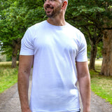 An upper body shot of a tall slim guy in a park wearing an XL tall and slim fitting mercerised t-shirt in white.