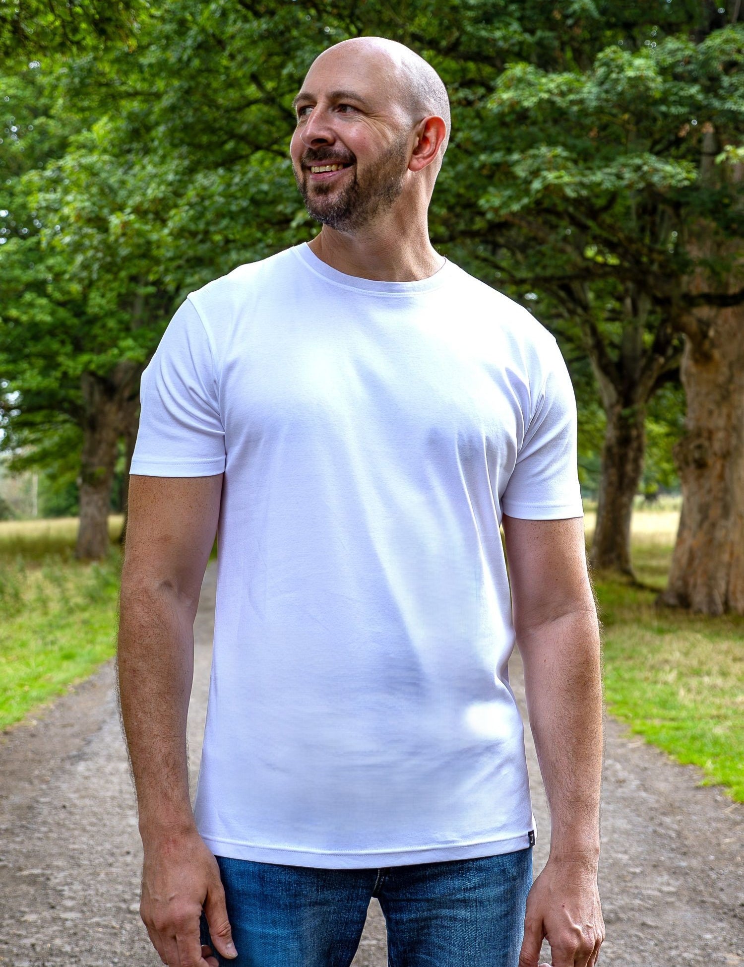 An upper body shot of a tall slim guy in a park wearing an XL tall and slim fitting mercerised t-shirt in white.
