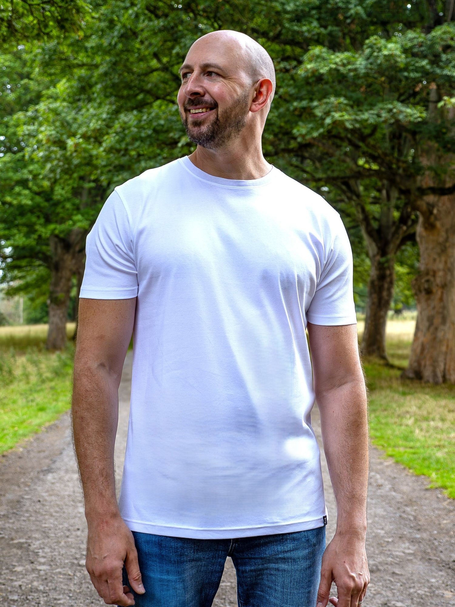 An upper body shot of a tall slim guy in a park wearing an XL tall and slim fitting mercerised t-shirt in white.