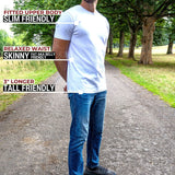A tall man standing on a park path wearing a white fitted short-sleeve t-shirt and blue jeans, with text callouts describing the shirt's fit and length.