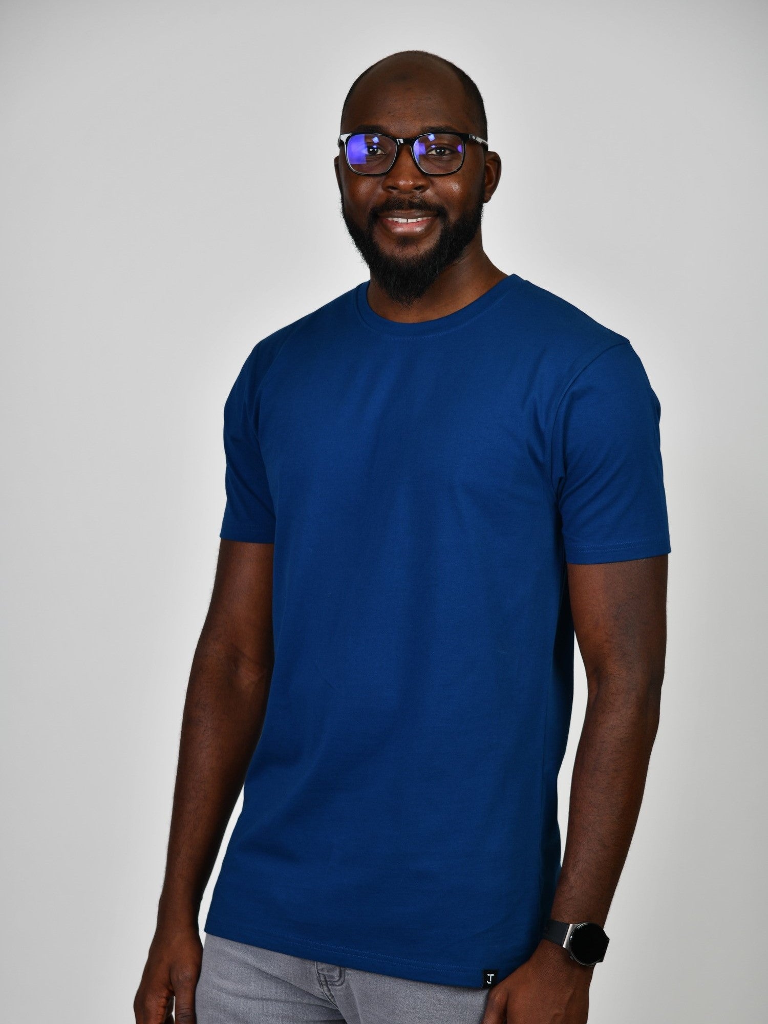 A tall and slim man in the studio standing in front of a light background. The smiling model is wearing an extra long slim navy blue t-shirt in a size large. The tall navy blue t-shirt features a 3" longer body, 100% organic cotton, and is soft & preshrunk. The navy blue t-shirt is ideal for tall slim men 6'2"+.