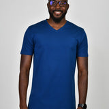 A tall and slim man in the studio standing in front of a light background. The smiling model is wearing an extra long slim navy blue v-neck t-shirt in a size large. The tall navy blue v-neck t-shirt features a 3" longer body, 100% organic cotton, and is soft & preshrunk. The navy blue v-neck t-shirt is ideal for tall slim men 6'2"+.