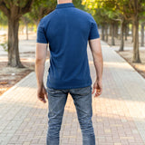 A shot from behind of a tall athletic guy in a park and wearing a navy XL tall polo shirt.