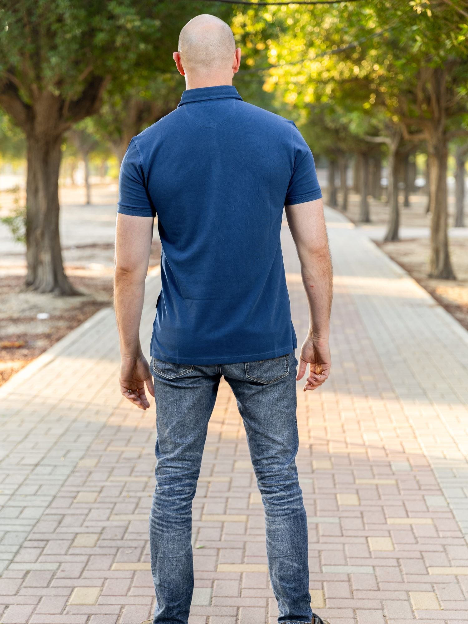 A shot from behind of a tall athletic guy in a park and wearing a navy XL tall polo shirt.