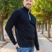 A tall and slim man standing on a path in  a park. The smiling model is wearing a black quarter zip sweatshirt. The tall black quarter zip sweatshirt features 2.5" longer sleeves, 100% organic french terry cotton, and is soft & comfy. It's  ideal for tall slim men 6'2"+.