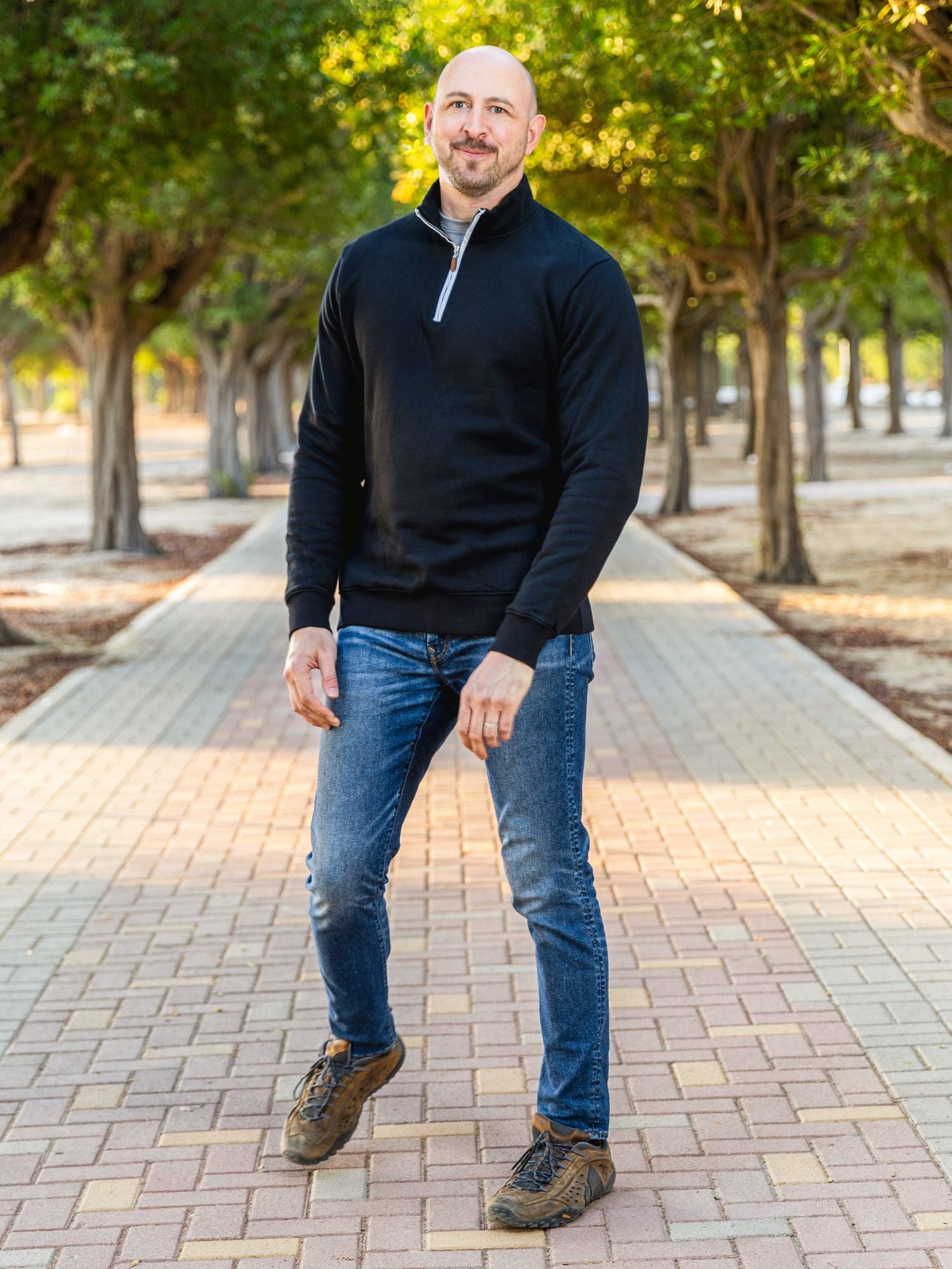 A tall slim guy wearing an XL tall black quarter zip sweatshirt in a park with his hands at his sides and smiling.