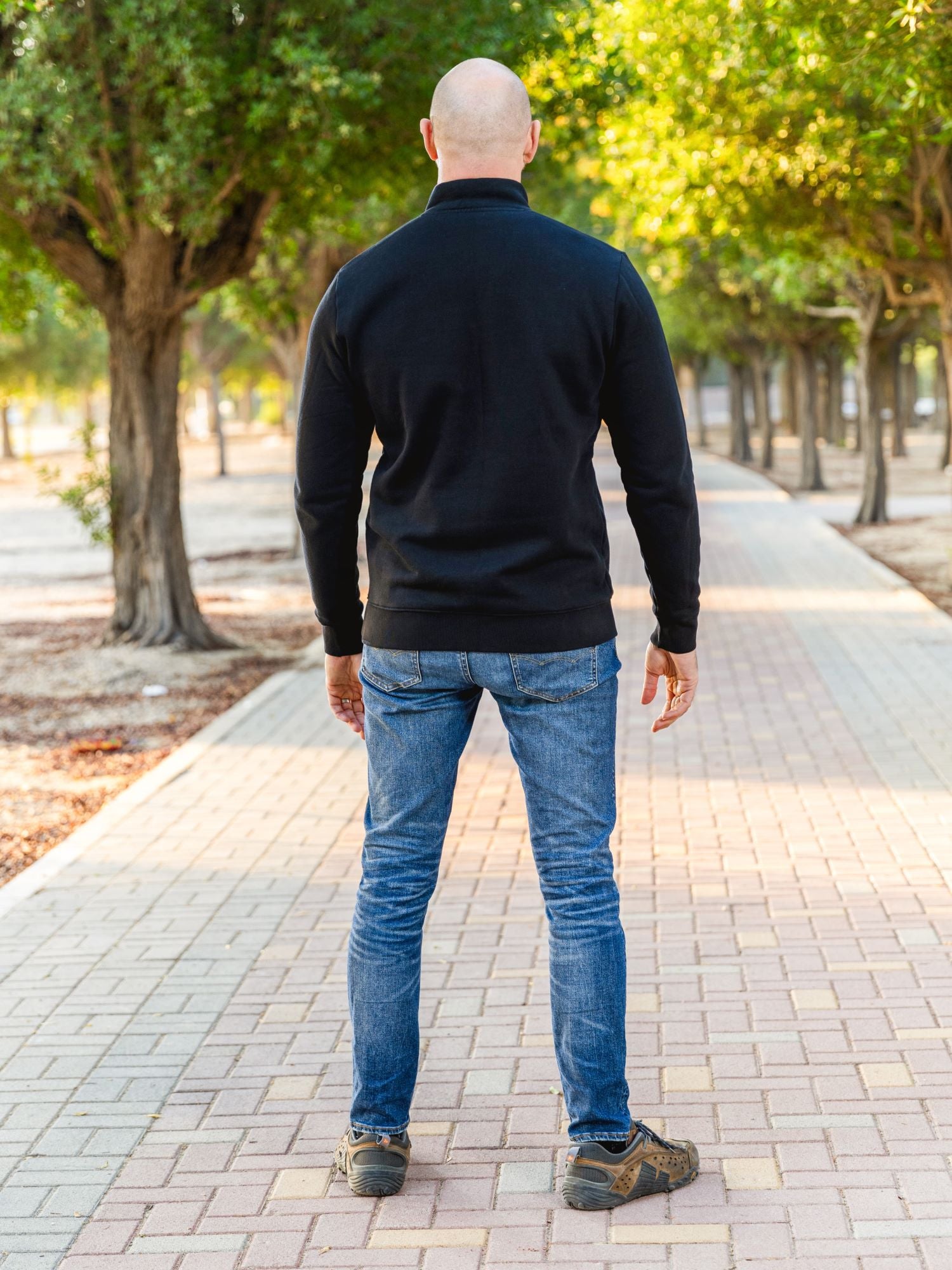 A shot from behind of a tall slim guy in a park wearing an XL tall extra long black quarter zip sweatshirt.