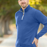 A tall and slim man standing on a path in  a park. The smiling model is wearing a cobalt quarter zip sweatshirt. The tall cobalt quarter zip sweatshirt features 2.5" longer sleeves, 100% organic french terry cotton, and is soft & comfy. It's  ideal for tall slim men 6'2"+.