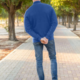 A shot from behind of a tall slim guy in a park wearing an XL tall extra long cobalt quarter zip sweatshirt.