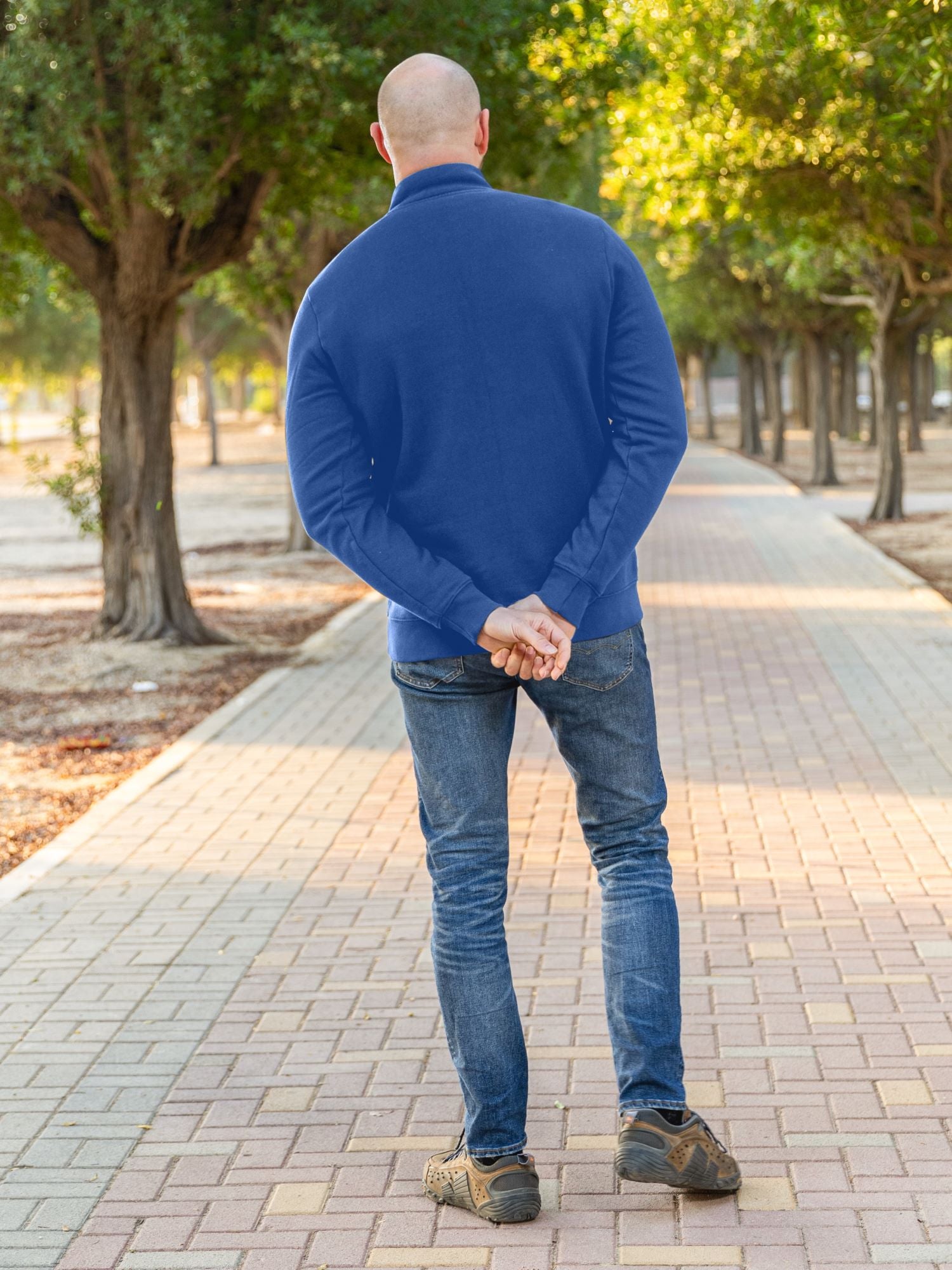 A shot from behind of a tall slim guy in a park wearing an XL tall extra long cobalt quarter zip sweatshirt.