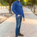 A tall slim guy wearing an XL tall cobalt quarter zip sweatshirt in a park with his hand in his pocket and smiling.