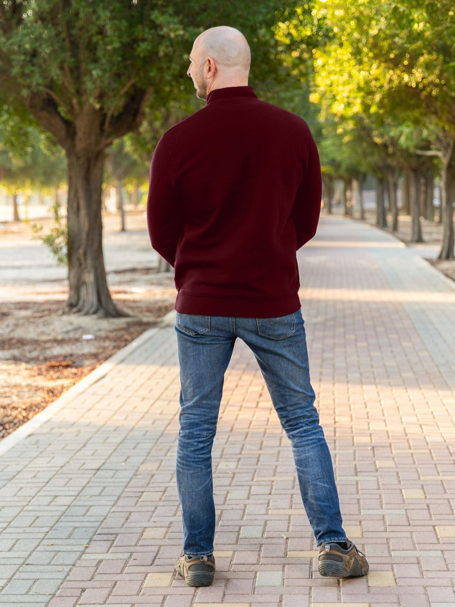 A shot from behind of a tall slim guy in a park wearing an XL tall extra long maroon quarter zip sweatshirt.