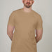 A tall and slim man in the studio standing in front of a light background. The model is wearing an extra long slim tan t-shirt in a size XL. The tan t-shirt features a 3" longer body, 100% organic cotton, and is soft & preshrunk. The tan t-shirt is ideal for tall slim men 6'2"+.