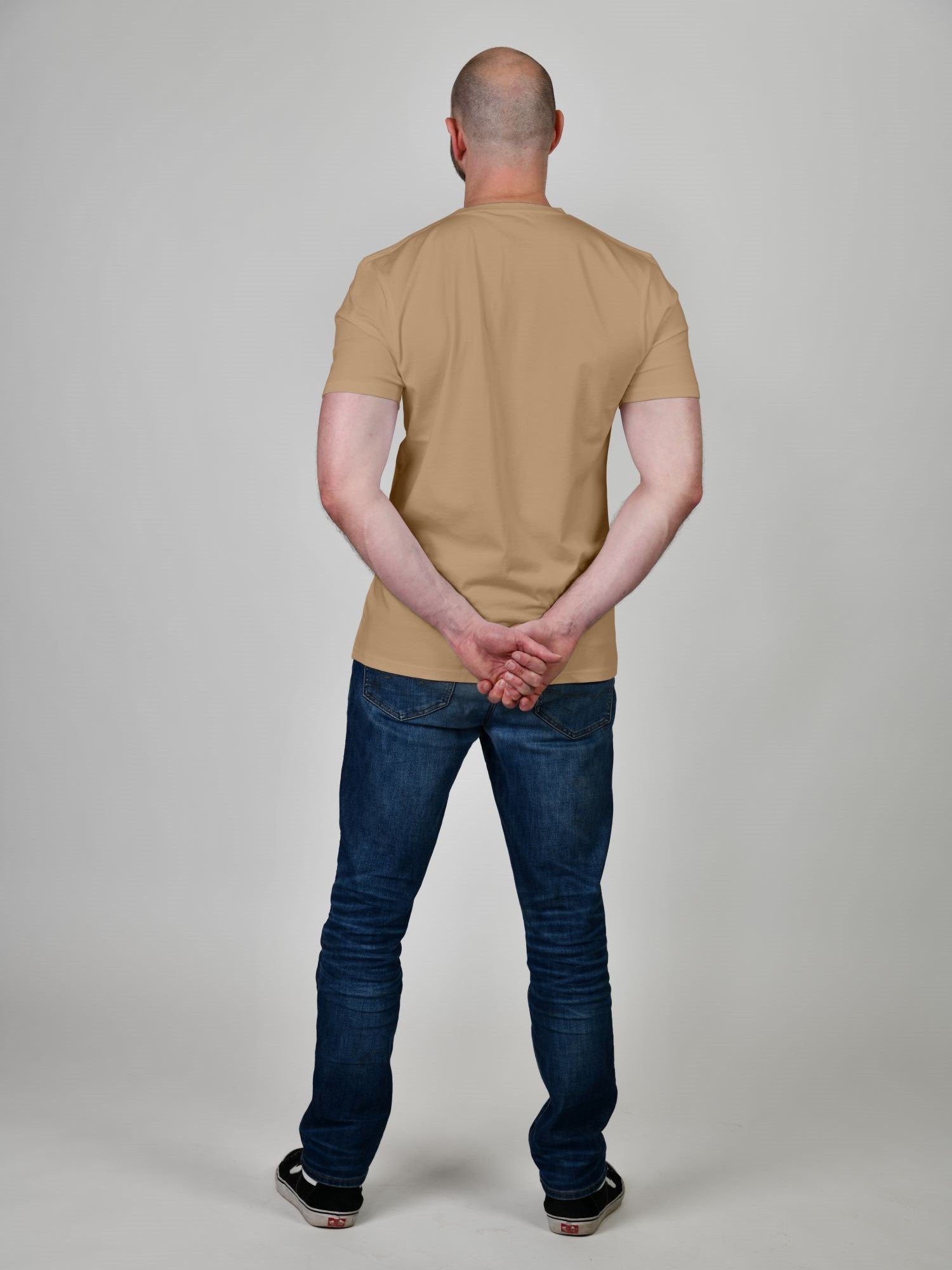 A shot from behind of a tall and slim guy in the studio and wearing a tan XL tall slim t-shirt.