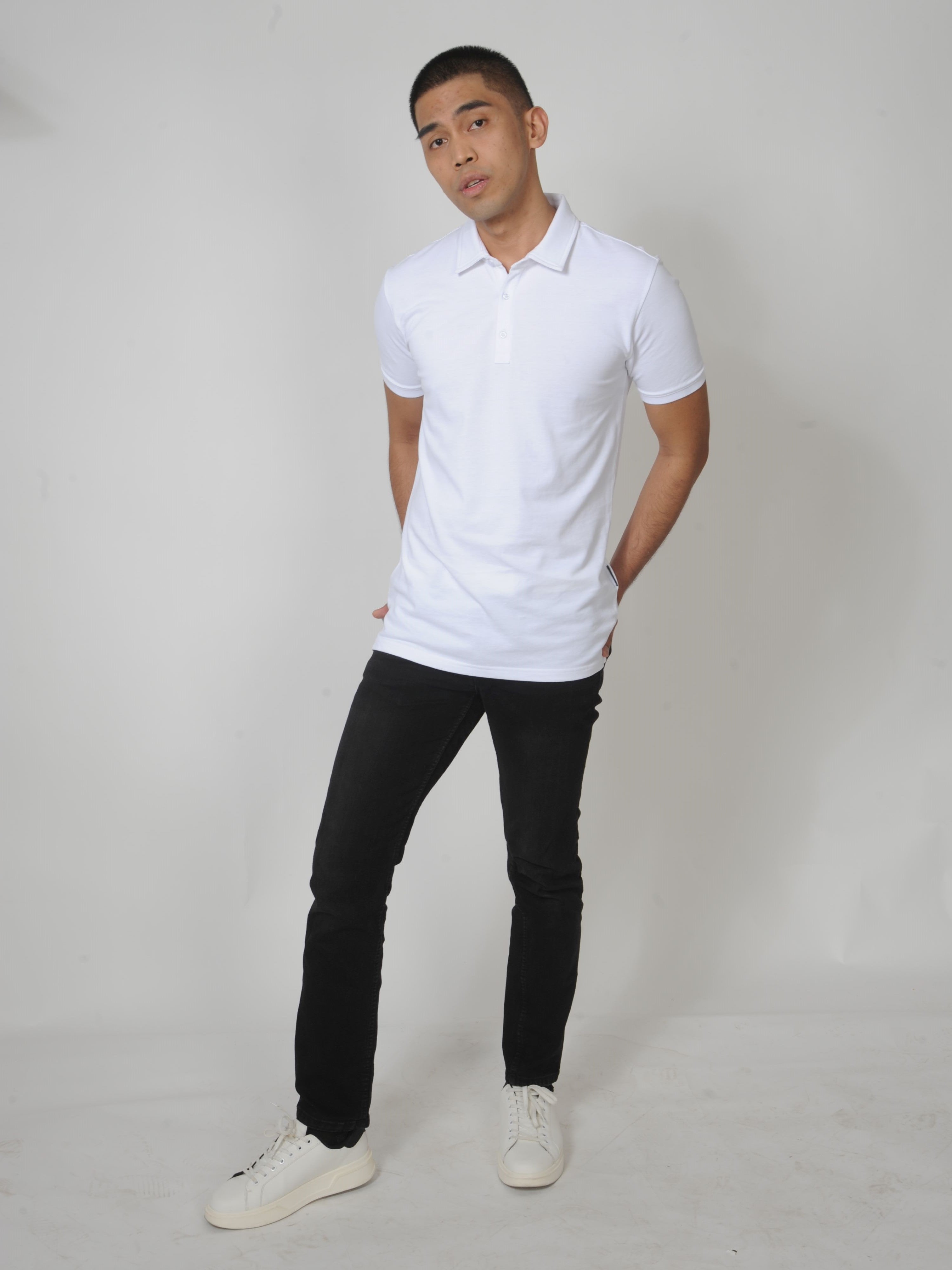 A head to toe shot of a tall slim guy in a studio and wearing a white M tall polo shirt.