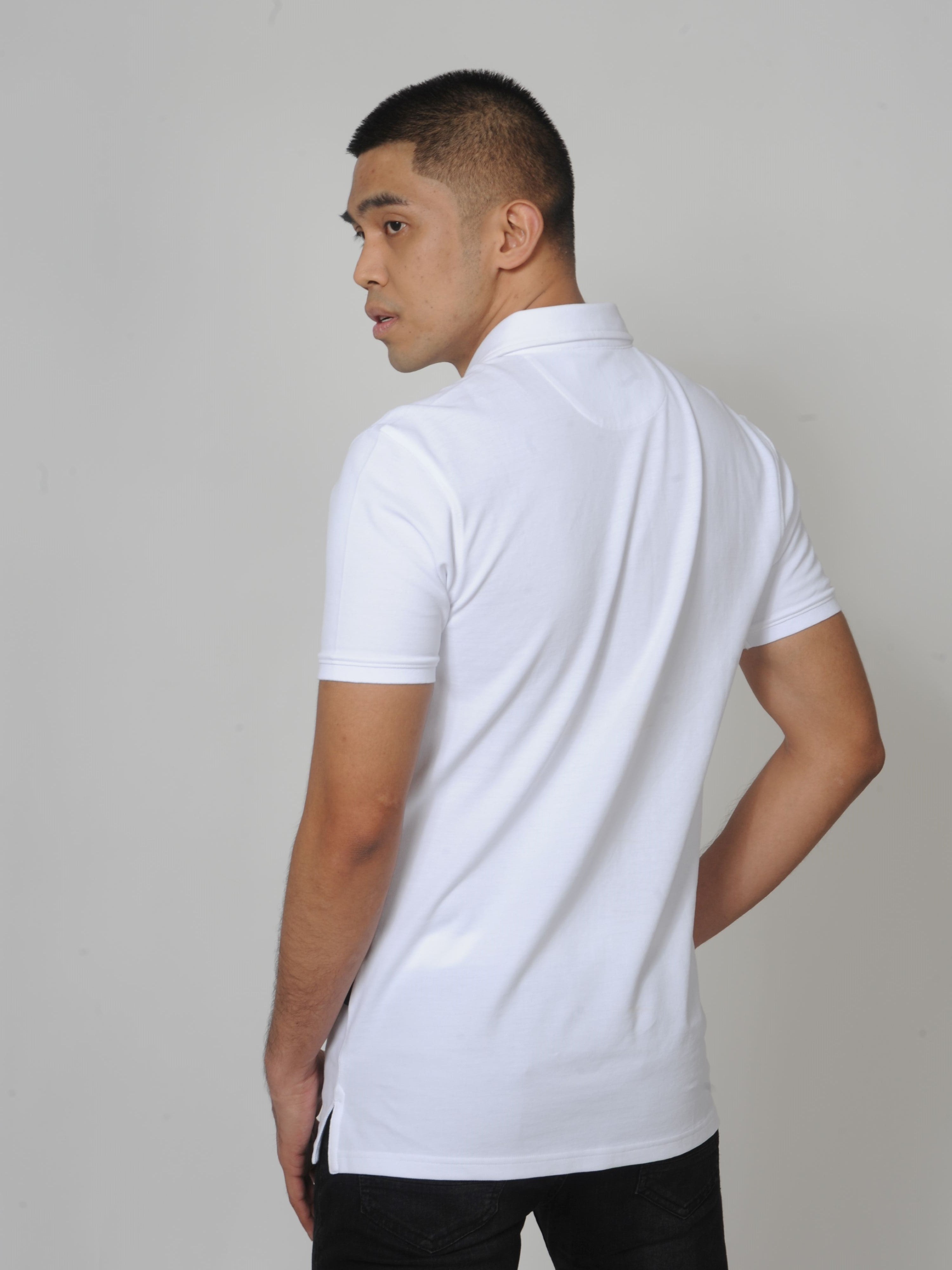 A shot from behind of a tall slim guy in a studio and wearing a white M tall polo shirt.