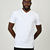 A tall and slim man in the studio standing in front of a light background with hands behind back. The model is wearing an extra long slim white v-neck t-shirt in a size large. The white v-neck t-shirt features a 3" longer body, 100% organic cotton, and is soft & preshrunk. The white v-neck t-shirt is ideal for tall slim men 6'2"+.
