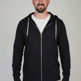 A tall slim guy standing against a wall, smiling and wearing an XL tall slim black zip up hoodie.