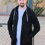A tall slim guy standing in a tennis court, smiling and wearing an XL tall slim black zip up hoodie.