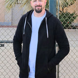 A tall slim guy standing in a tennis court, smiling and wearing an XL tall slim black zip up hoodie.