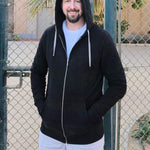 A tall slim guy wearing an XL tall black hoodie with hands in pockets and hood on, standing in a tennis court.