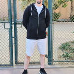 A tall and athletic guy wearing an XL tall black hoodie, standing in a tennis court, hands behind back and smiling.