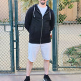 A tall and athletic guy wearing an XL tall black hoodie, standing in a tennis court, hands behind back and smiling.