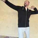 A tall slim man wearing a tall black full zip hoodie and striking a super star pose and laughing.