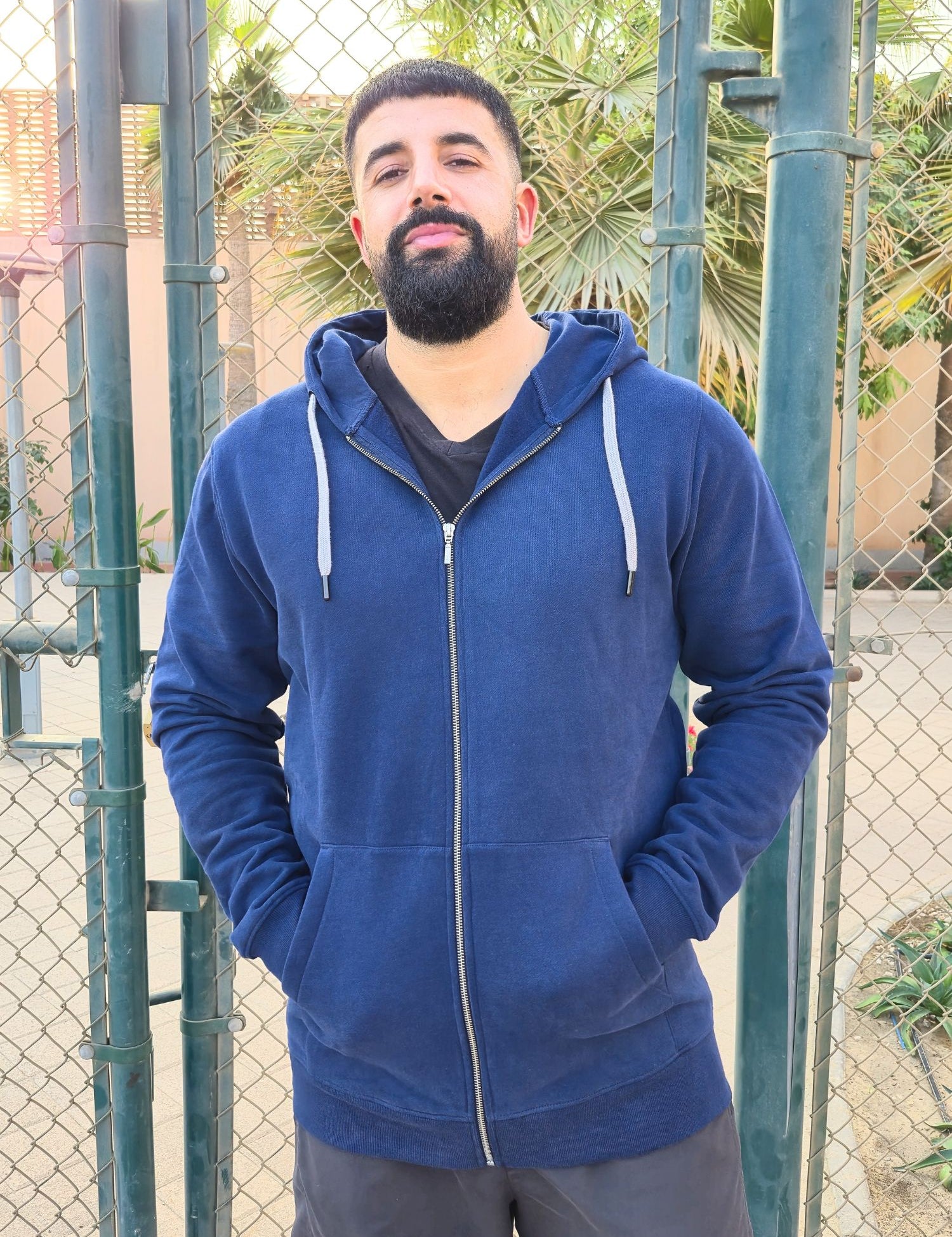 A tall and broad guy standing in a tennis court and wearing a 2XL Tall dark navy zip-up hoodie.