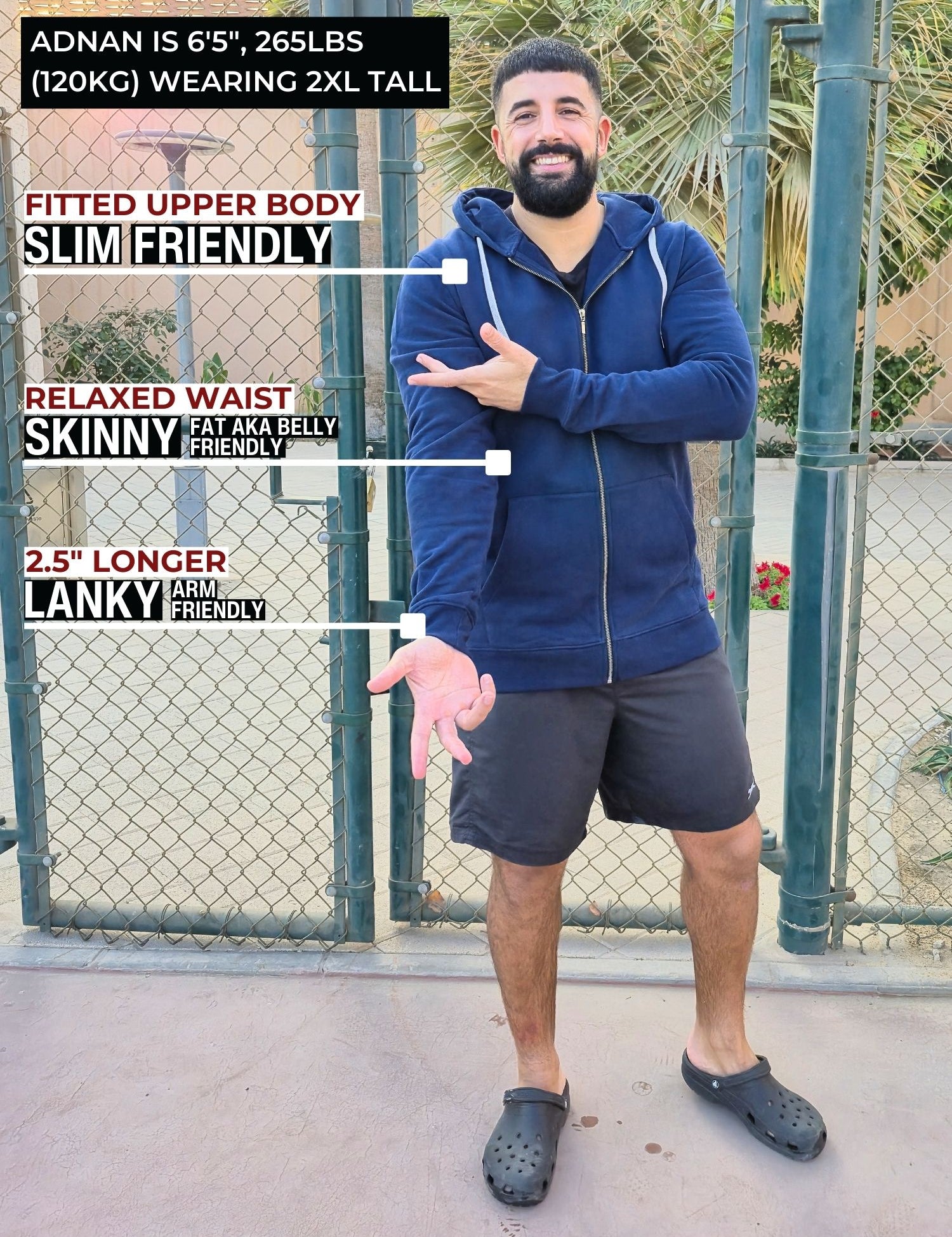 A head to toe shot of a tall and broad guy standing in a tennis court and wearing a 2XL Tall dark navy zip-up hoodie.