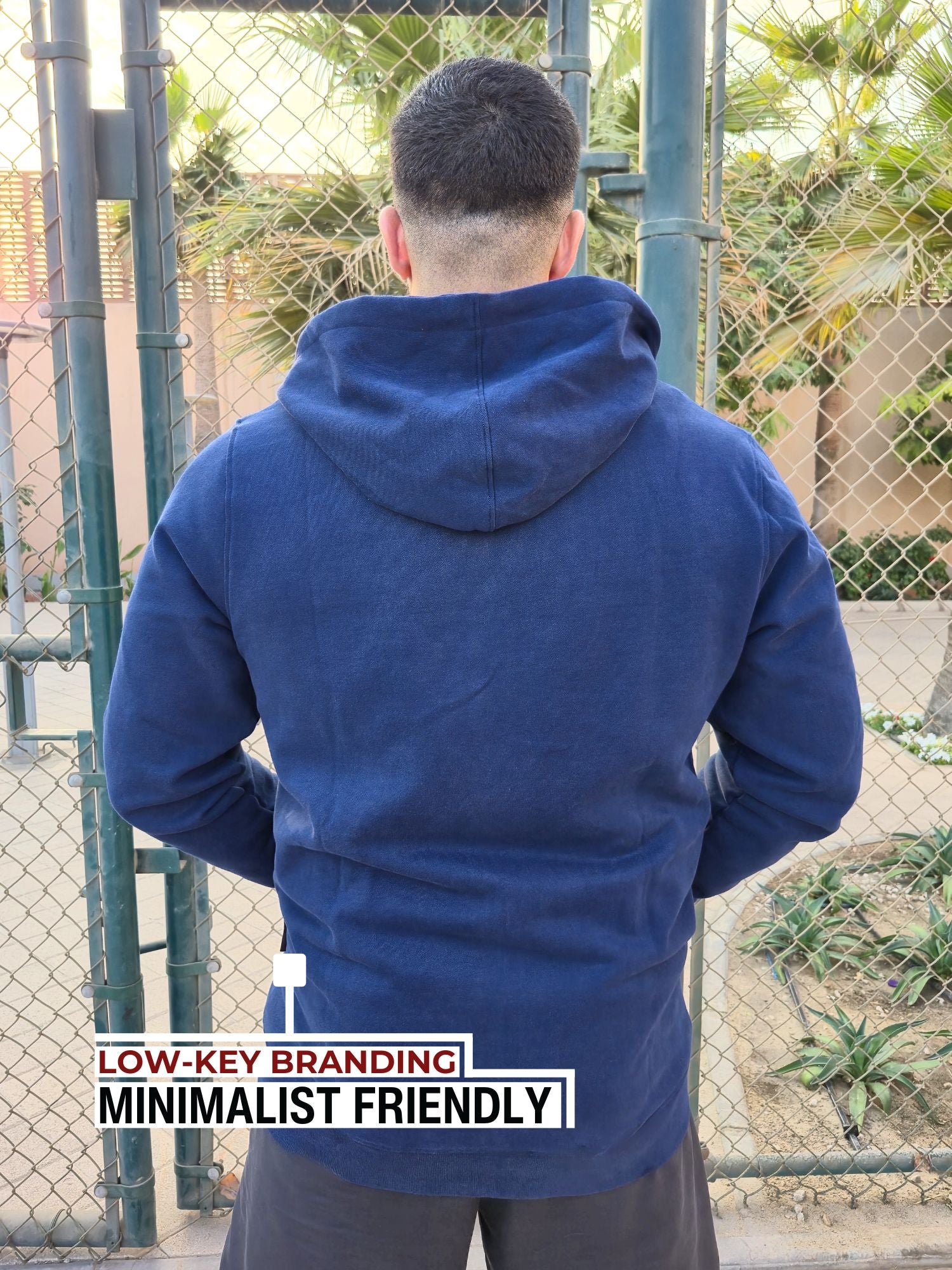 A shot from behind of a tall and broad guy standing in a tennis court and wearing a 2XL Tall dark navy zip-up hoodie.