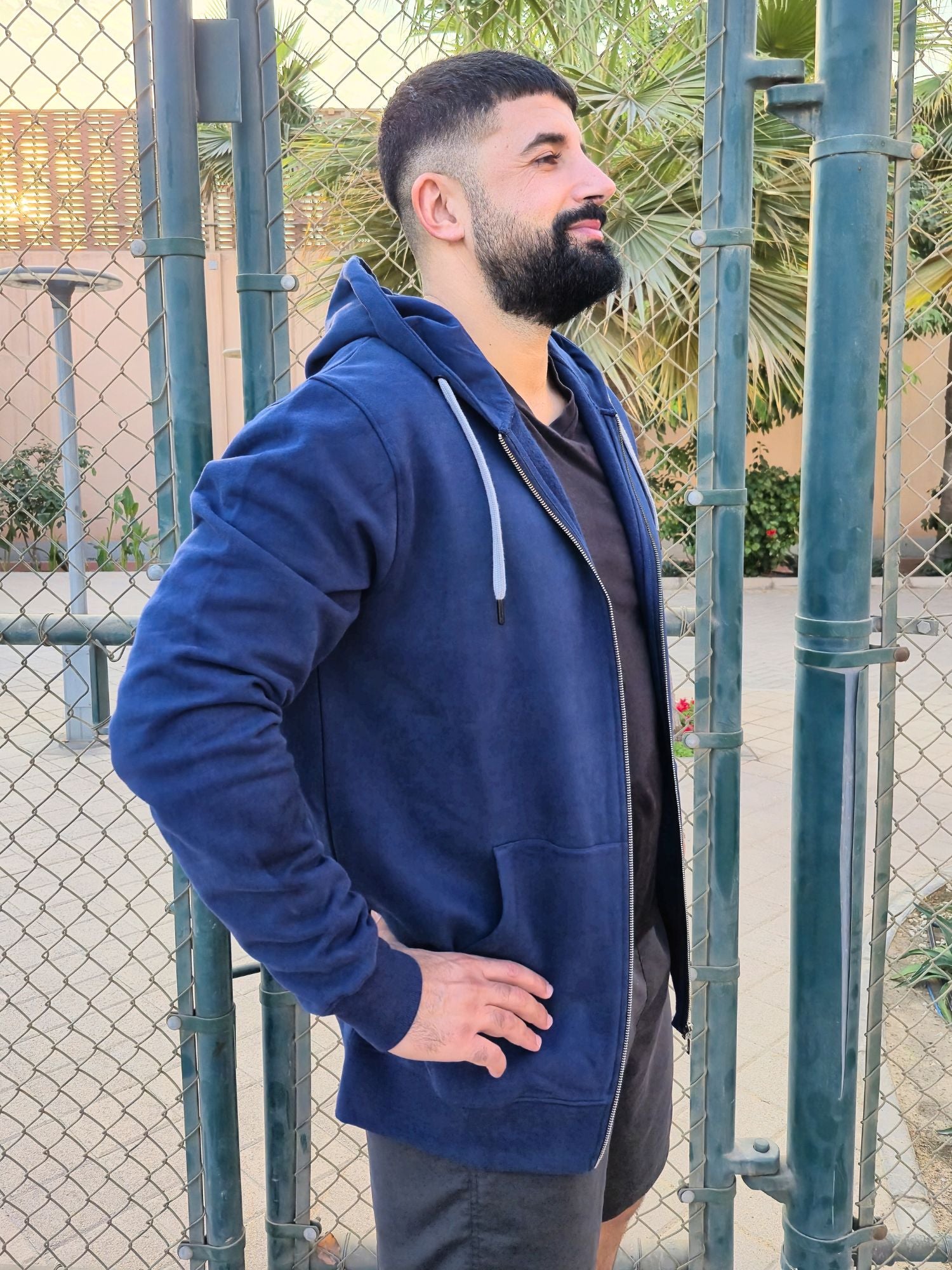 A side on shot of a tall and muscular guy standing in a tennis court and wearing an XL tall slim dark navy hoodie.
