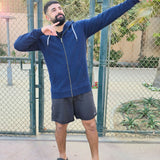 A tall and muscular guy standing in a tennis court and wearing an XL tall dark navy hoodie.