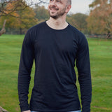 A tall and slim man standing in a park. The smiling model is wearing a black long-sleeve tall t-shirt. The tall black long-sleeve t-shirt features a 2.5" longer sleeves, 100% organic cotton, and is soft & preshrunk. The black long-sleeve t-shirt is ideal for tall slim men 6'2"+.