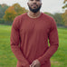 A tall and slim man standing in a park. The smiling model is wearing a dark orange long-sleeve tall t-shirt. The tall dark orange long-sleeve t-shirt features a 2.5" longer sleeves, 100% organic cotton, and is soft & preshrunk. The dark orange long-sleeve t-shirt is ideal for tall slim men 6'2"+.