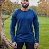 A tall and slim man standing in a park. The smiling model is wearing a navy blue long-sleeve tall t-shirt. The tall navy blue long-sleeve t-shirt features a 2.5" longer sleeves, 100% organic cotton, and is soft & preshrunk. The navy blue long-sleeve t-shirt is ideal for tall slim men 6'2"+.