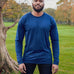 A tall and slim man standing in a park. The smiling model is wearing a navy blue long-sleeve tall t-shirt. The tall navy blue long-sleeve t-shirt features a 2.5" longer sleeves, 100% organic cotton, and is soft & preshrunk. The navy blue long-sleeve t-shirt is ideal for tall slim men 6'2"+.