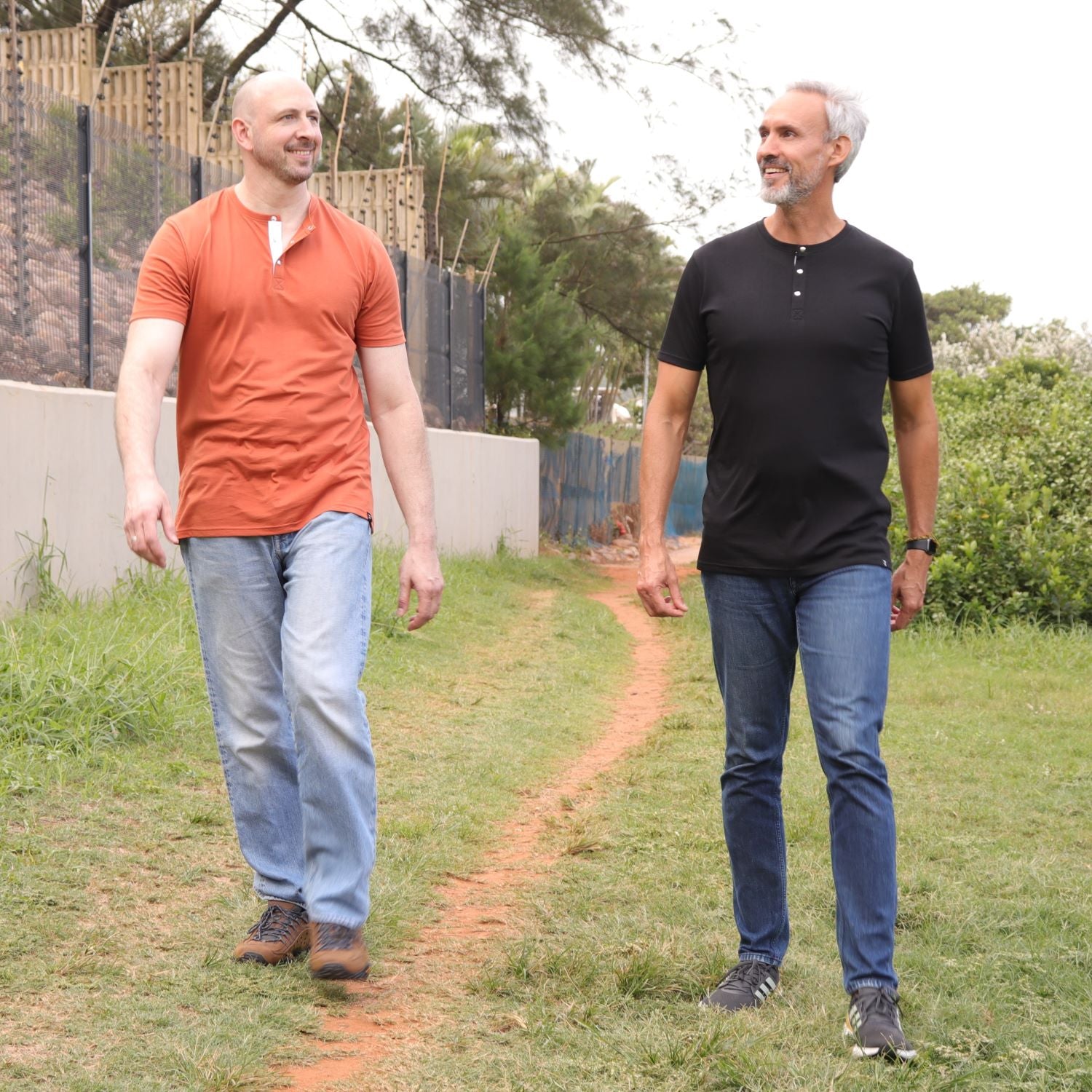 Two tall slim guys wearing black and brown tall henley shirts in a park.