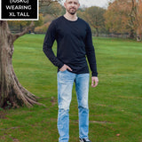 A head to toe shot of a tall athletic guy in a park wearing a black long sleeve tall t-shirt.