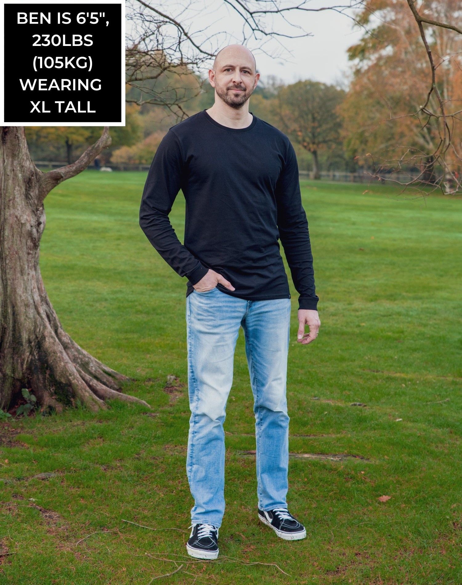 A head to toe shot of a tall athletic guy in a park wearing a black long sleeve tall t-shirt.