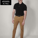 A head to toe shot of a tall slim guy wearing a black XL tall polo shirt tucked into a brown belt.