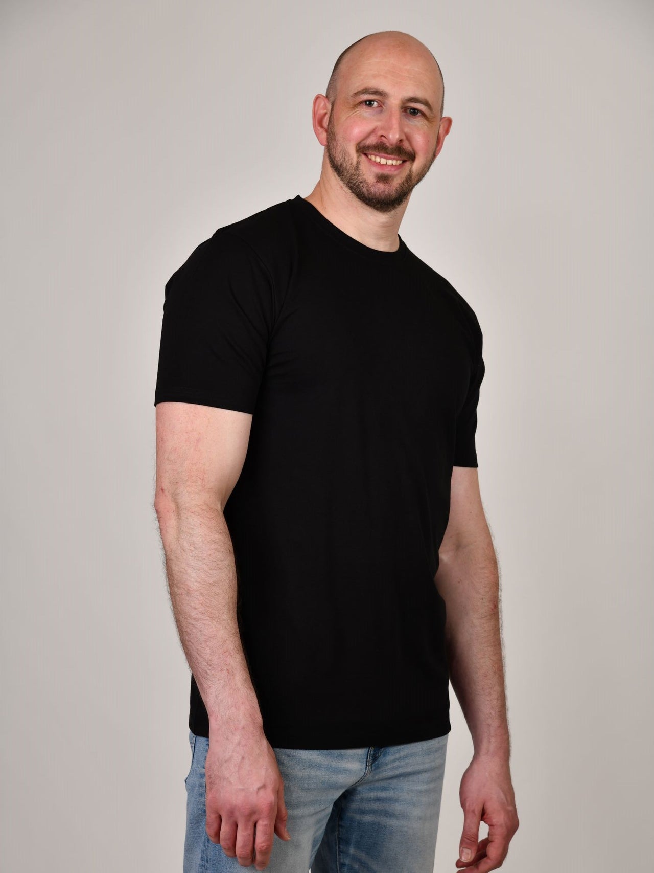 A tall and slim guy in the studio wearing a black XL tall slim t-shirt.
