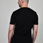 A shot from behind of a tall and slim guy in the studio and wearing a black XL tall slim t-shirt.