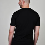 A shot from behind of a tall and slim guy in the studio and wearing a black XL tall slim t-shirt.